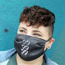 Load image into Gallery viewer, Rebellion 99 member shown modeling a black Rebellion 99 reusable mask. 99 is features prominently above the crest. Art Deco and poppy accents are semi-transparent in background of mask.

