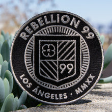 Load image into Gallery viewer, 3.5&quot; embroidered Rebellion 99 crest shown. Silver metallic thread is embroidered onto black twill background.
