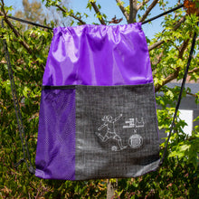 Load image into Gallery viewer, Purple drawstring backpack is shown in front of green trees.
